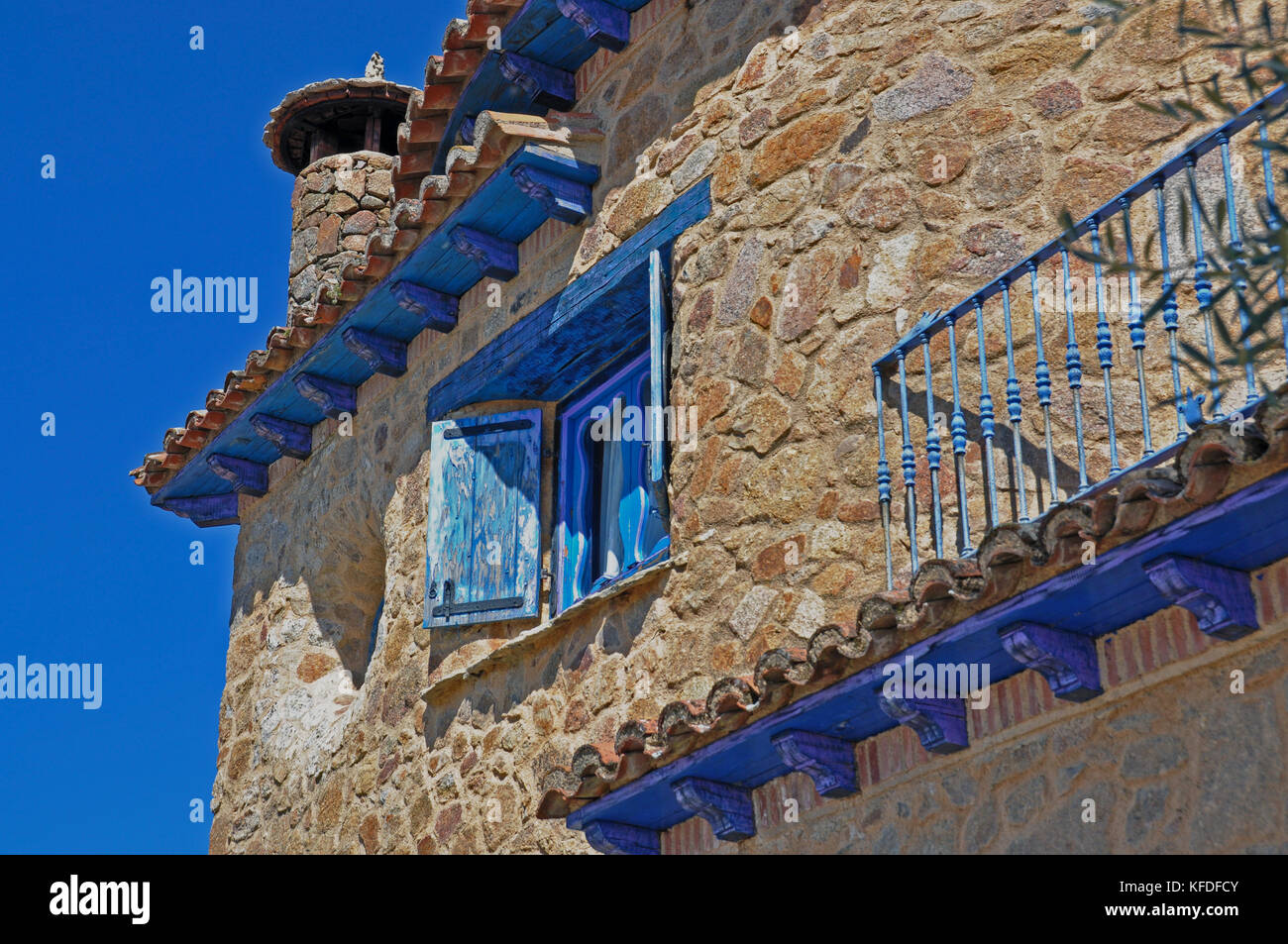 Un angolo superiore di una casa costruita di marrone e grigio pietra con elementi in legno dipinto di blu brillante matching luminoso cielo blu. C'è un turno camino. Foto Stock