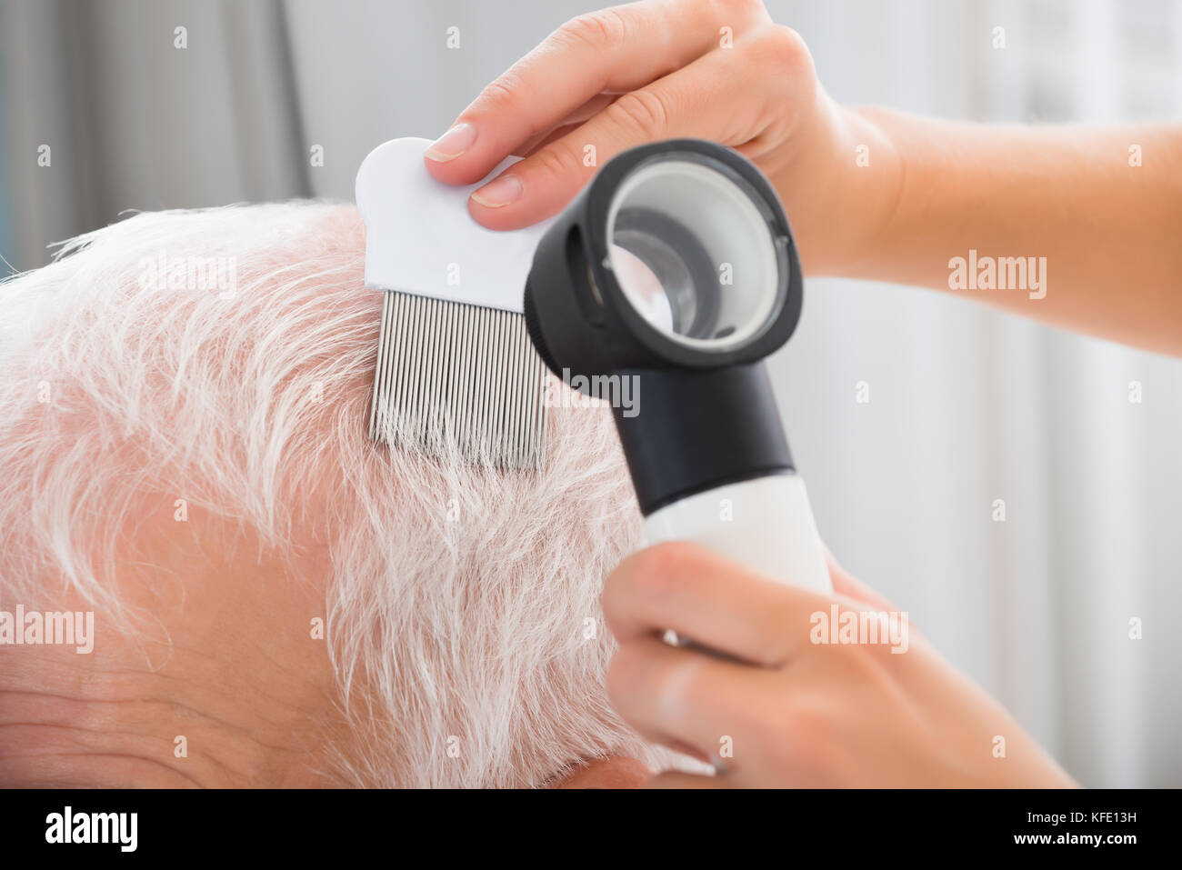 Close-up di medico con pettine e dermatoscope facendo il trattamento del paziente anziano i capelli Foto Stock