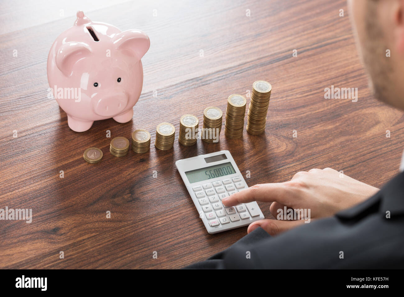 Close-up di imprenditore utilizzando la calcolatrice con piggybank e monete impilate su scrivania Foto Stock