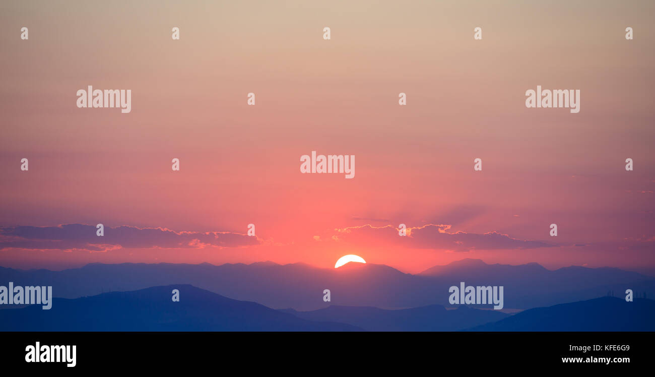 Bel tramonto sul cielo arancione sulle montagne sullo sfondo. Il sole è nel mezzo. Foto Stock