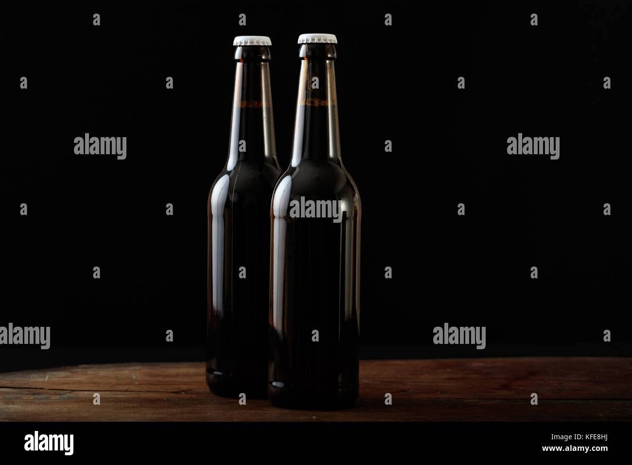 Primo piano di due aperti di bottiglie di birra isolato su una panca in legno, sfondo nero Foto Stock