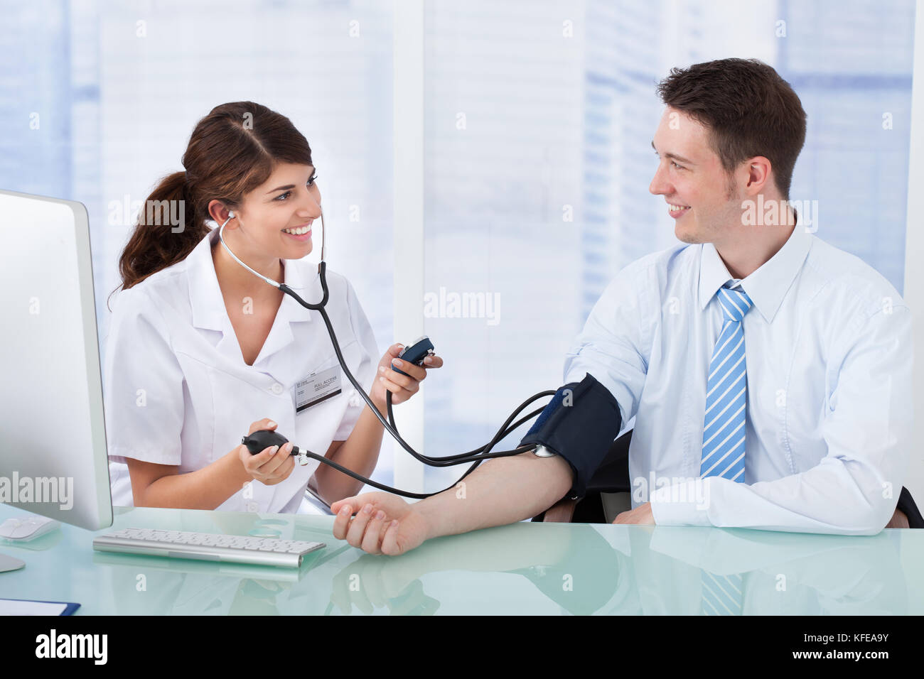 Giovani donne medico controllando la pressione del sangue di imprenditore in clinica Foto Stock