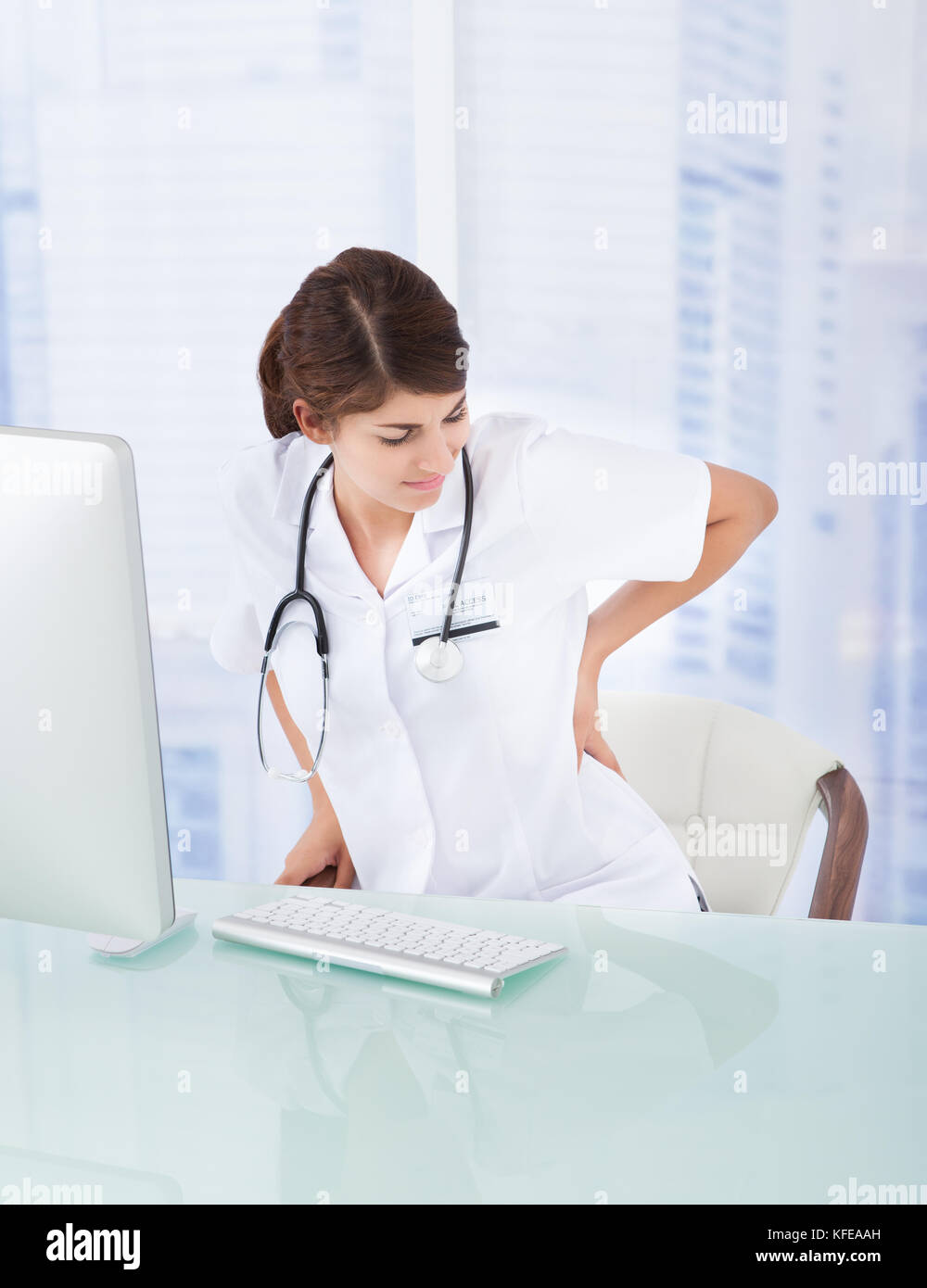 Triste medico donna con mal di schiena a computer desk in clinica Foto Stock