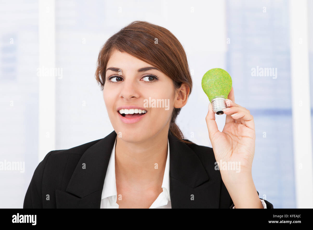 Ritratto di felice imprenditrice tenendo la luce verde lampadina in ufficio Foto Stock