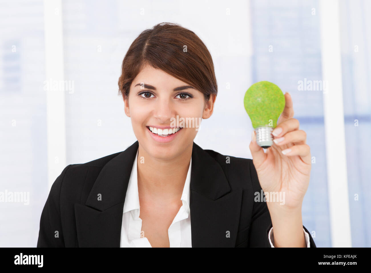 Ritratto di felice imprenditrice tenendo la luce verde lampadina in ufficio Foto Stock