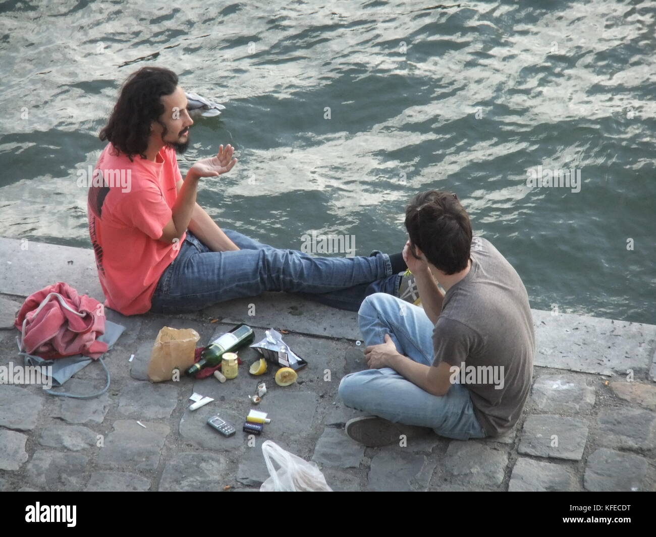 Due amici a parlare e bere vino e mangiare e fumare sul retro del Fiume Senna a Parigi Foto Stock