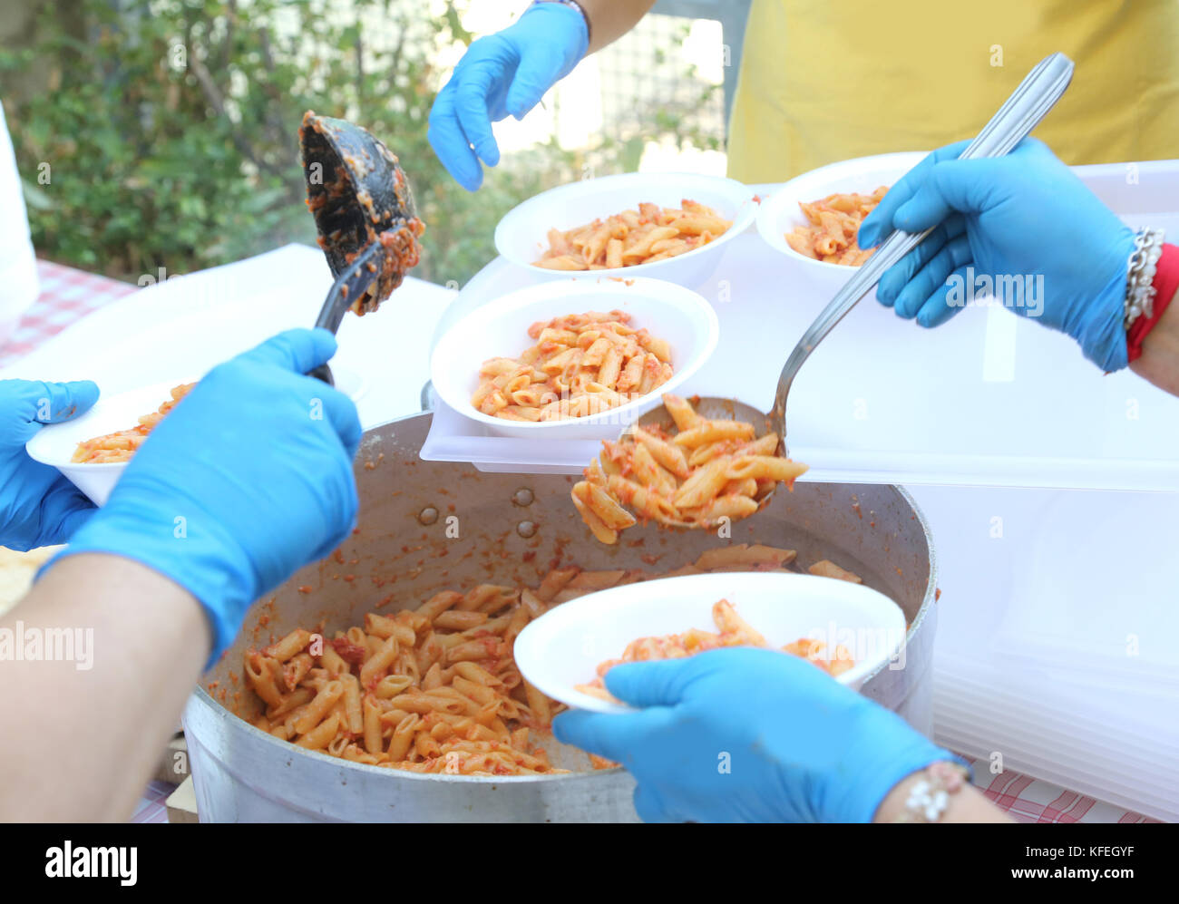 Le mani con guanti in lattice blu dei cuochi durante la distribuzione dei pasti di pasta con salsa di pomodoro Foto Stock