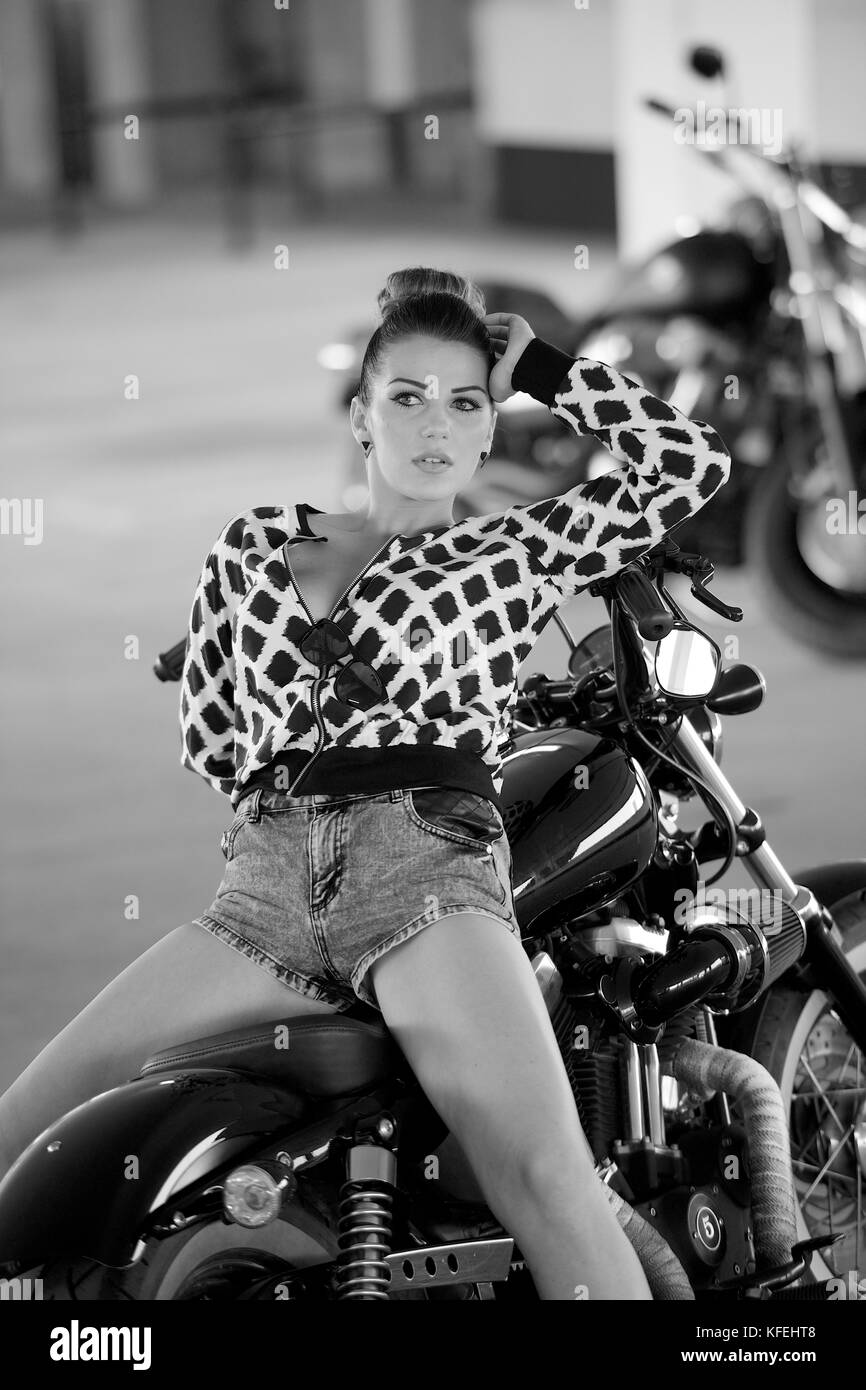 Bella bruna ragazza indossare pantaloncini corti e una camicia con un nero Harley Davidson Moto Foto Stock