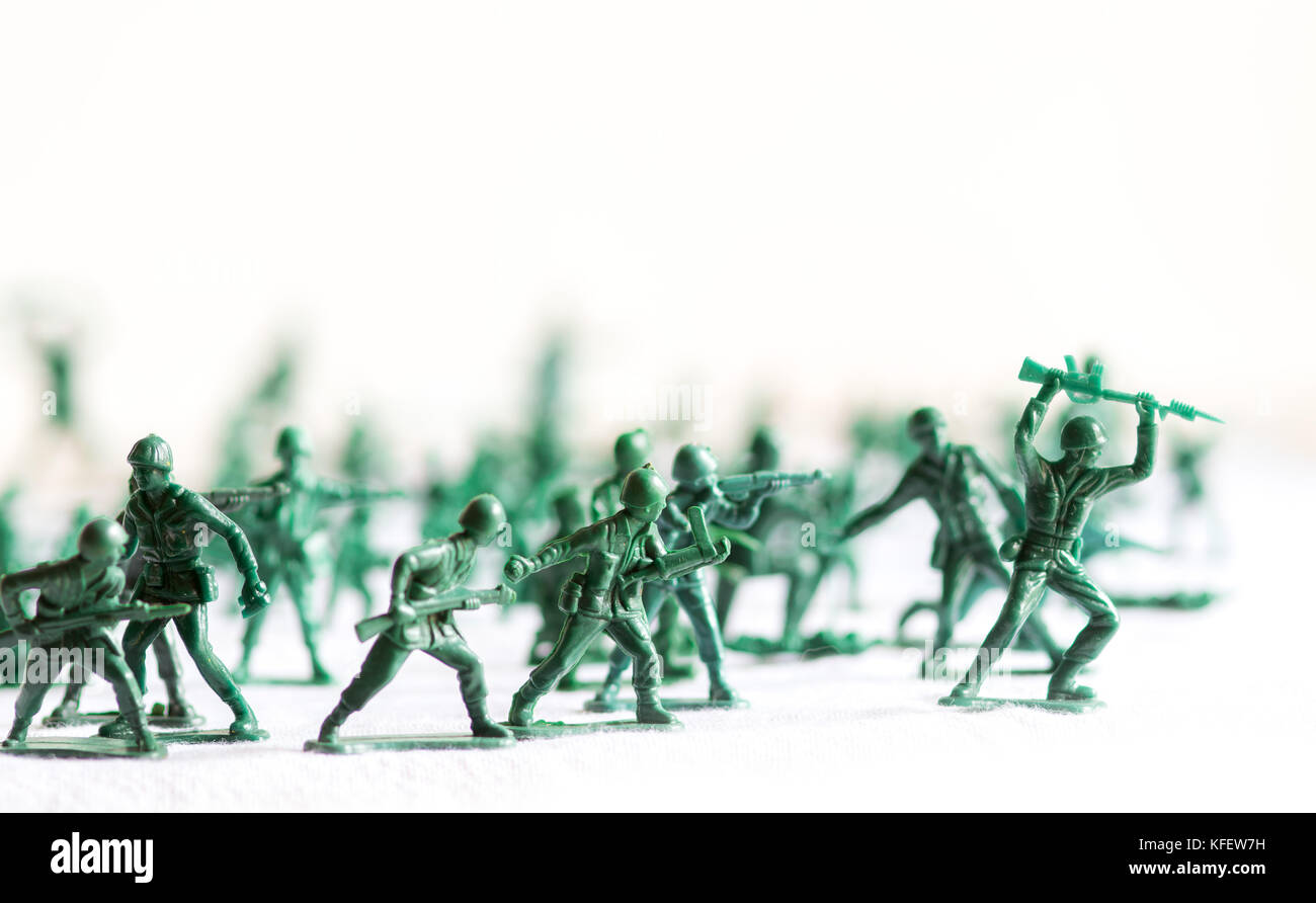 Molti esercito verde giocattolo di plastica soldati hanno organizzato sulla parte superiore di una superficie bianca e sfondo, isolata, con fuori fuoco soldati di plastica nel contesto Foto Stock