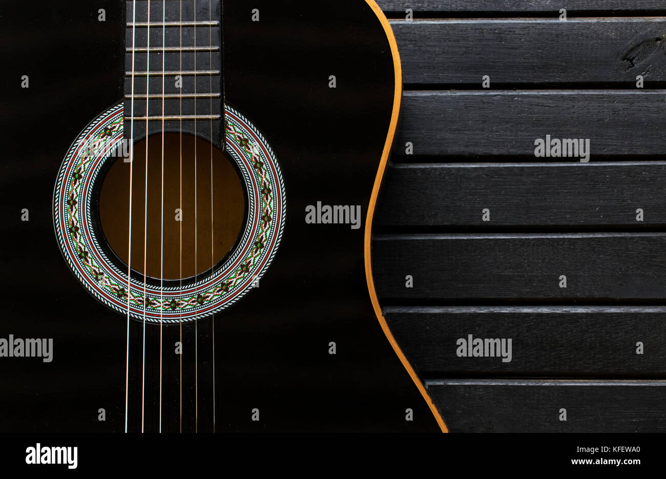 Nero chitarra acustica corpo closeup, verticale, su di un legno nero lo sfondo della tabella, con un sacco di texture, che mostra la forma di chitarra e spazio di copia Foto Stock