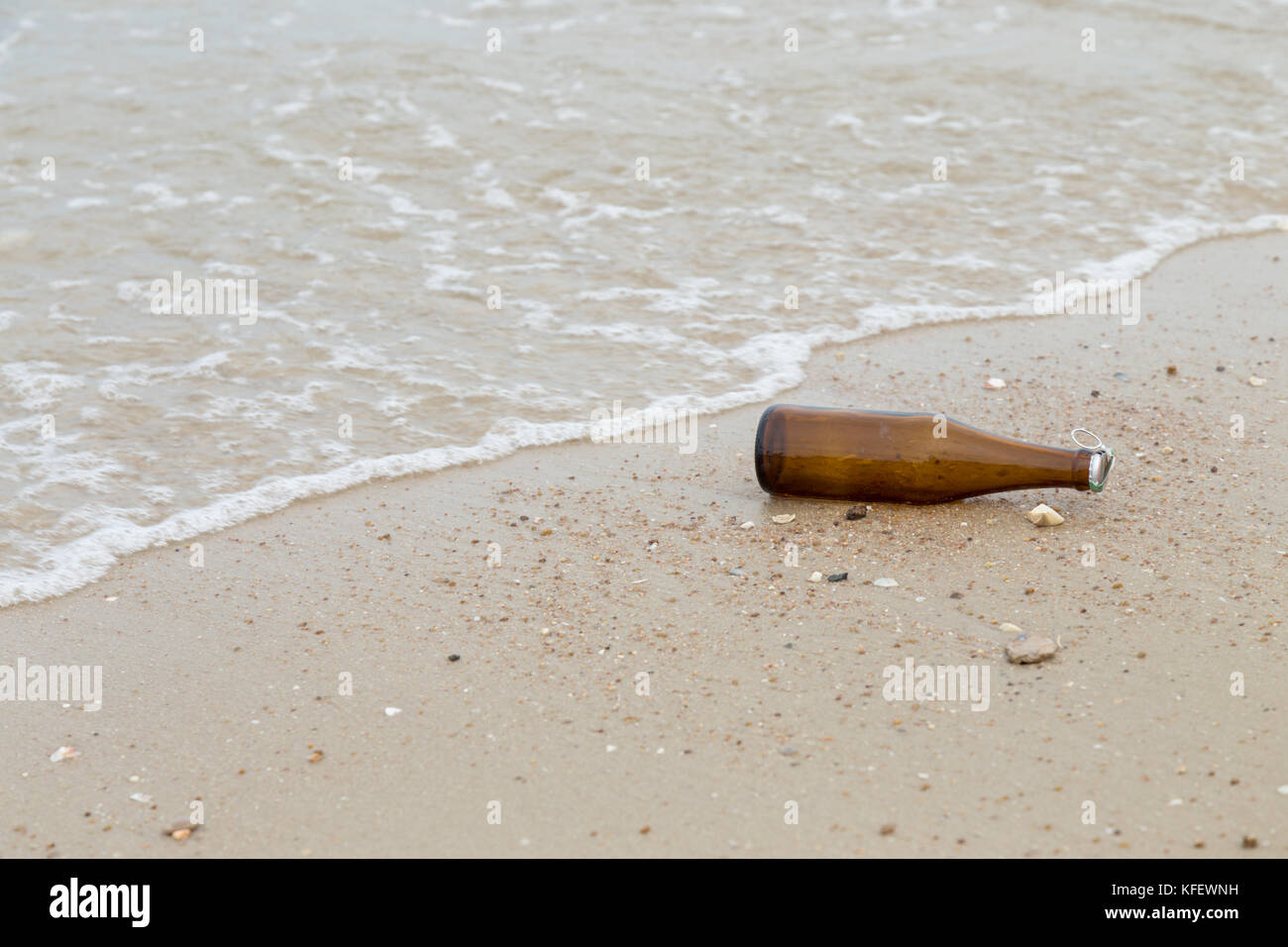 Svuotare la bottiglia di vetro che giace sulla spiaggia di sabbia con sea wave acqua. foto con copia spazio. Foto Stock