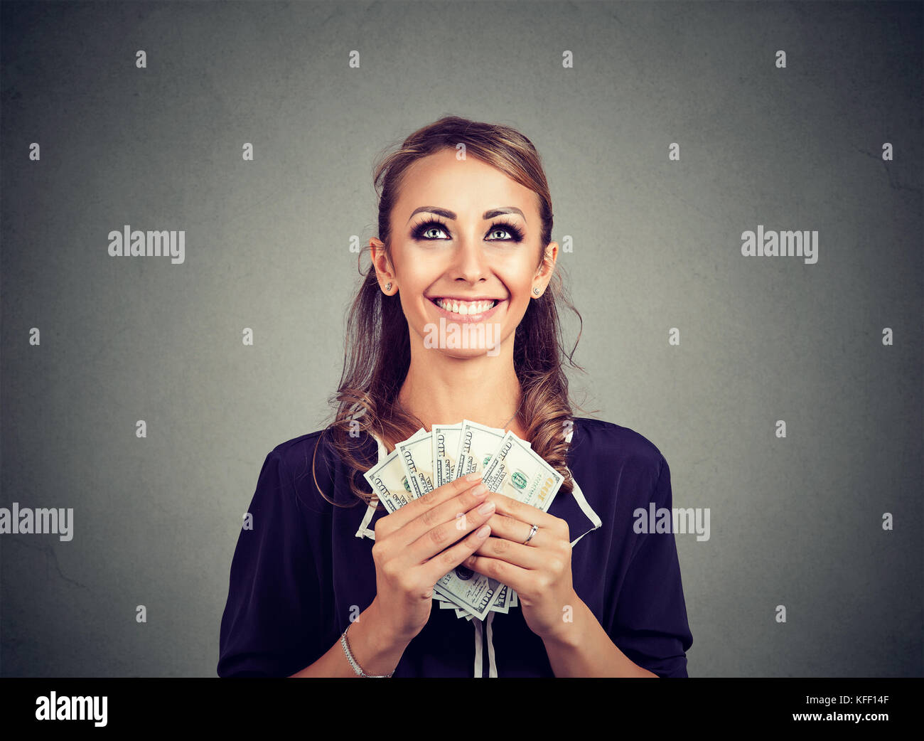 Donna felice holding US Dollar Bills su sfondo grigio e cercando fantasticando su come spendere Foto Stock