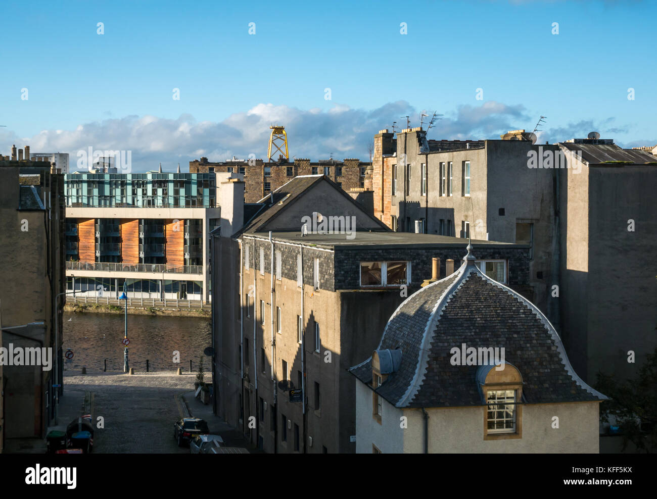 Vista sui tetti delle antiche e moderne costruzioni in Leith, Edimburgo, Scozia, con enormi giallo turbina eolica piattaforma in distanza Foto Stock