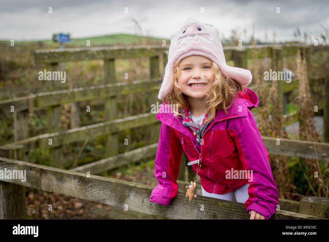 Giovane donna bambino con un grande sorriso vestito in autunno inverno abiti godendo la vita all'aperto su una passeggiata in campagna. Ella è arrampicata su una recinzione. Foto Stock
