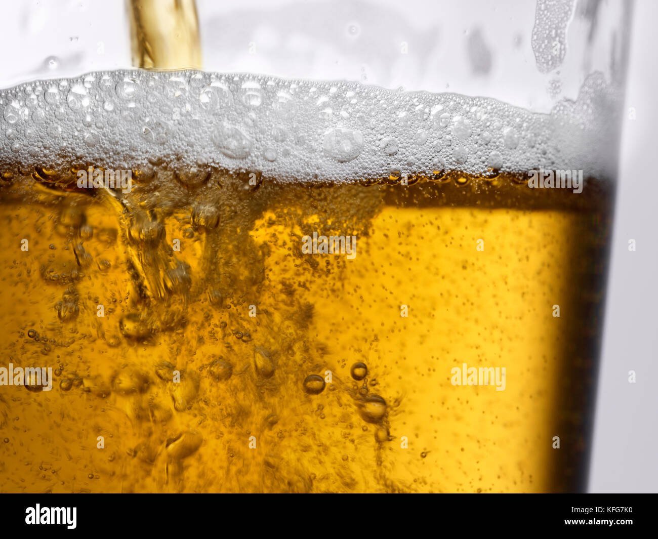 Primo piano azione girato di ambra oro per spillare la birra in vetro trasparente con bolle e di schiuma di testa Foto Stock