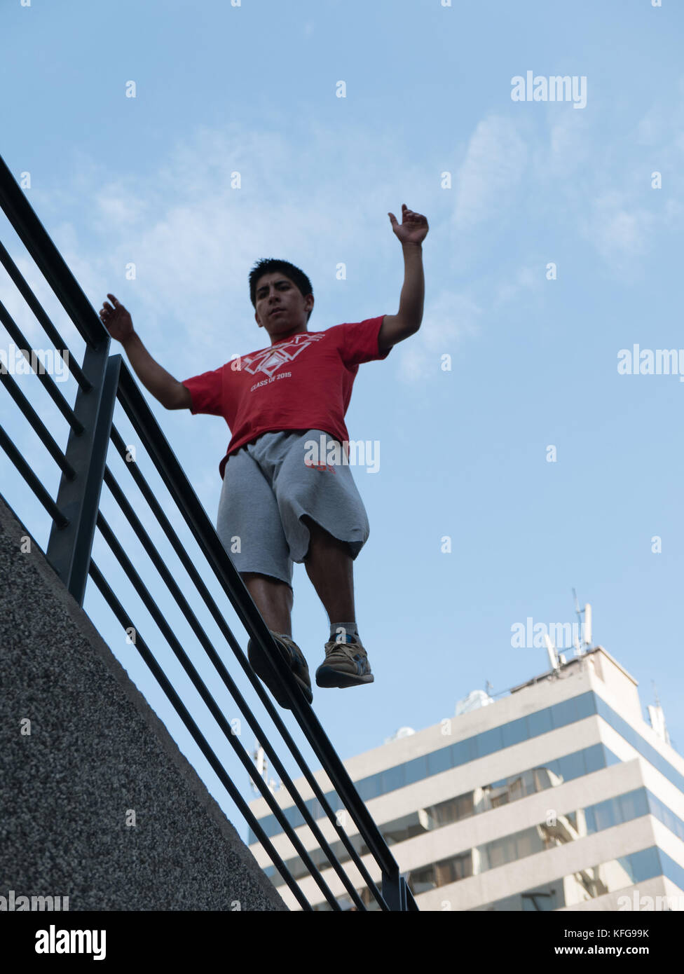 Giovane uomo in Santiago del Cile impegnato nel parkour in equilibrio su un corrimano in alto sopra la terra con il cielo blu e alto edificio bianco in background Foto Stock