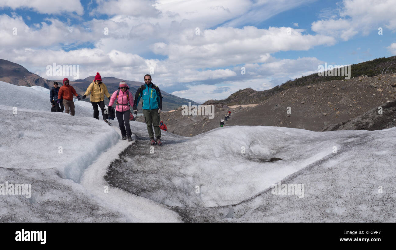 Guide leader di un gruppo di colorfully vestito i turisti in una breve escursione sul ghiacciaio con il cielo blu, il paesaggio glaciale, correnti e vette glaciali Foto Stock