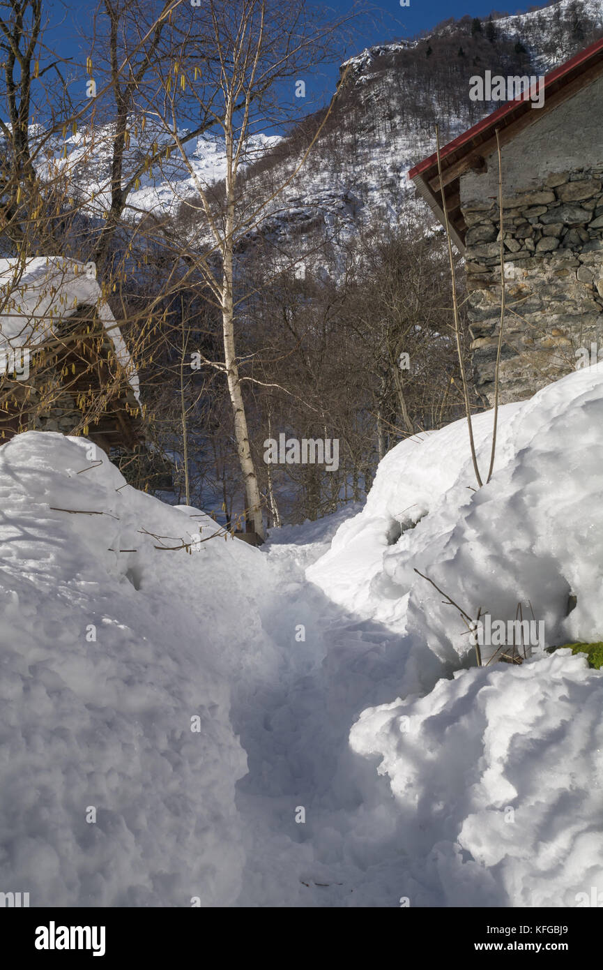 Sentiero alpino con vecchi edifici dopo una nevicata in mattinata di cammino nelle Alpi coperte da neve Foto Stock