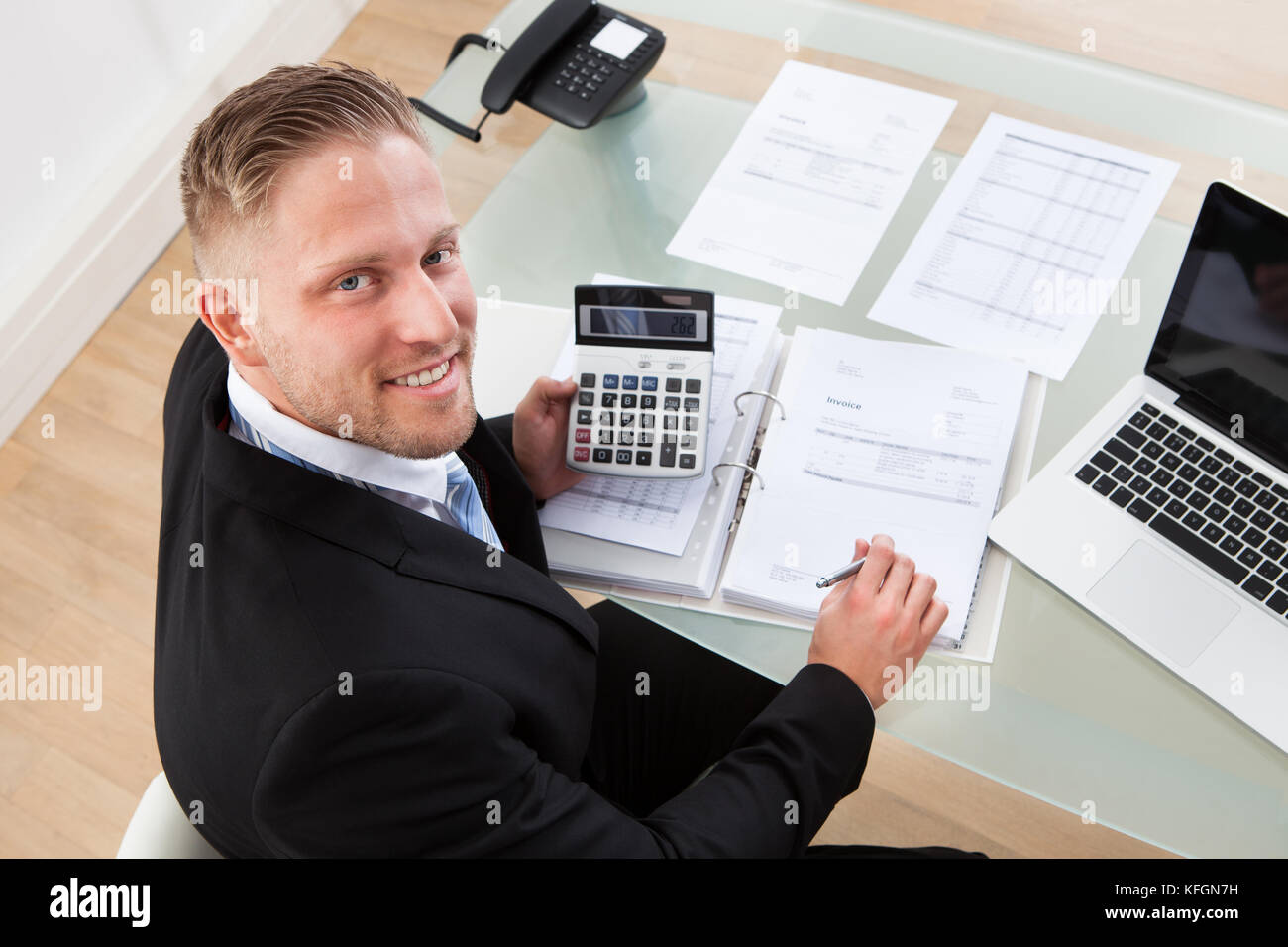 Vista da sopra di un gentile uomo d affari al lavoro in ufficio cercando fino dalla sua scrivania presso la telecamera con un sorriso Foto Stock