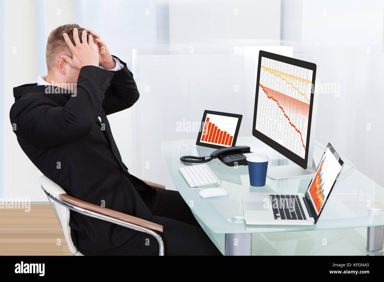 Imprenditore disperato di fronte a perdite finanziarie seduto alla sua scrivania consultazione tre grafici su monitor diversi tutti scenda in rosso Foto Stock