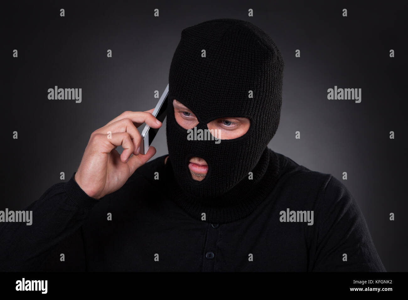 Ladro di un passamontagna e abito nero in piedi al buio utilizzando un  furto di telefono cellulare o un terrorista attivando una bomba in remoto  Foto stock - Alamy
