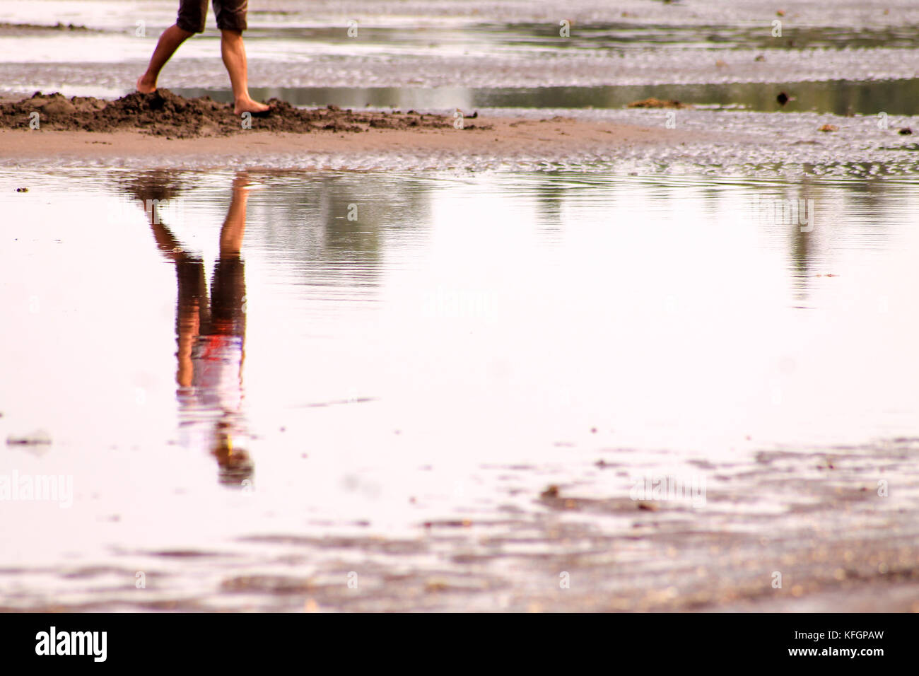 Riflessione di un uomo che cammina da solo su una superficie d'acqua che mostra il concetto di allontanamento sociale e di autoisolamento dovuto la pandemia covid-19 Foto Stock