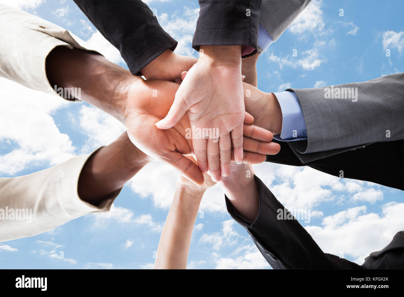 Primo piano di business multietnica le mani sulla parte superiore di ogni altro che simboleggia l'unità contro sky Foto Stock