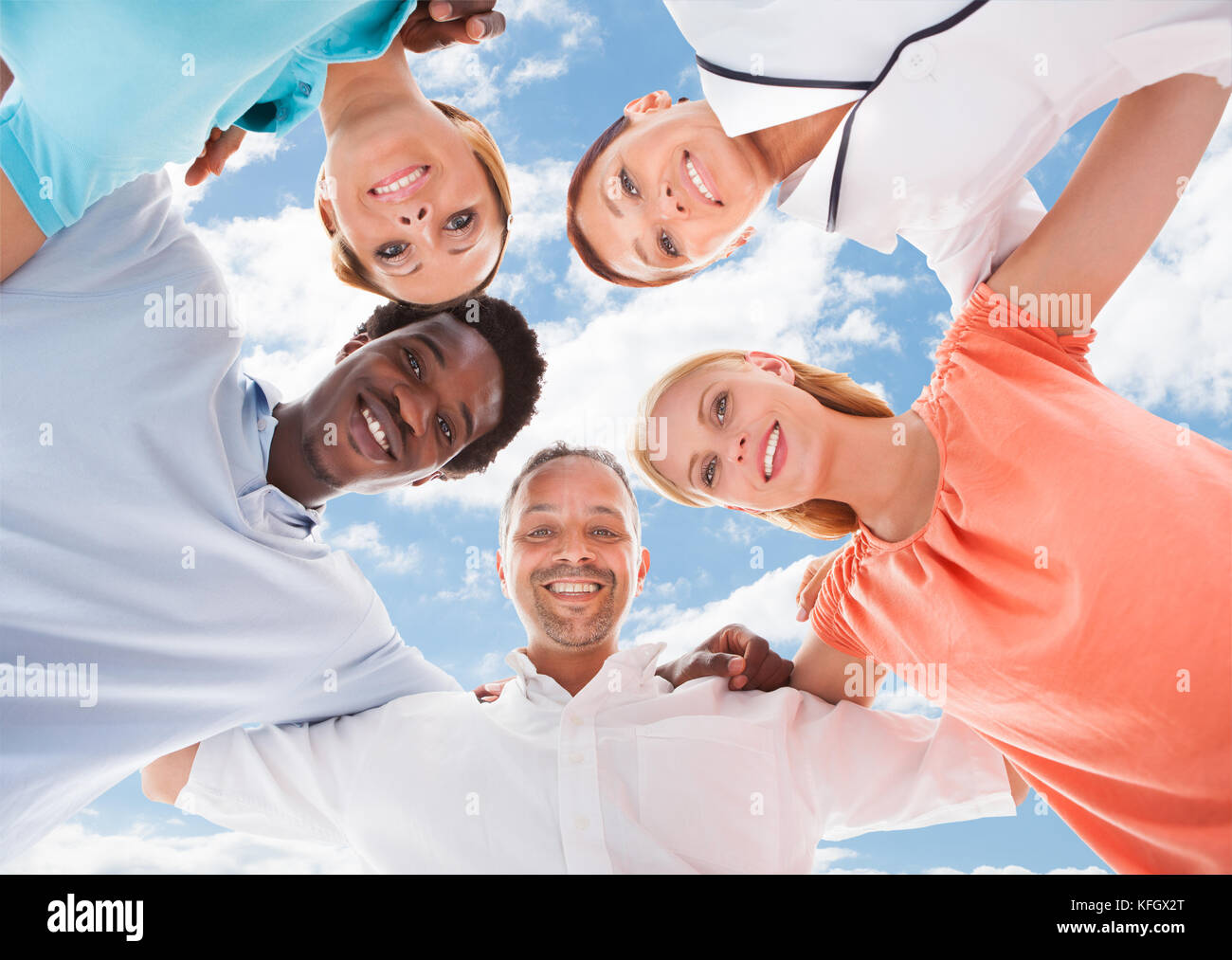 Direttamente sotto il ritratto di business multietnica persone formando huddle contro sky Foto Stock