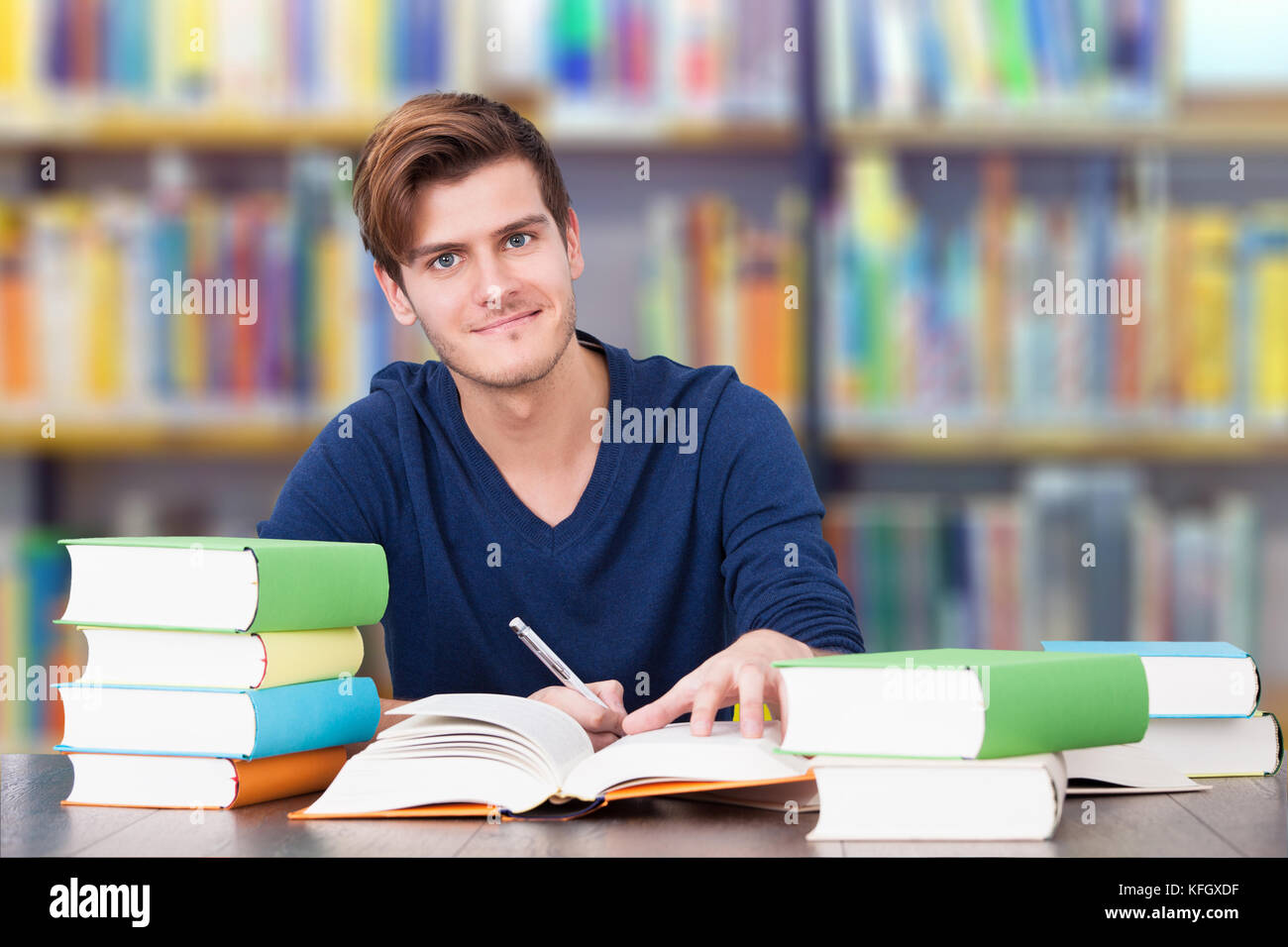 Ritratto di maschio sorridente studente universitario che studia a tavola in biblioteca Foto Stock