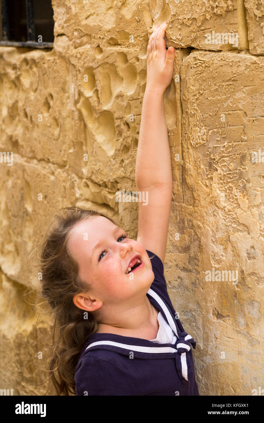Giovane ragazza / bambino / bambini / bambino di età compresa tra i 5 anni e su una vacanza in famiglia esamina l'antico muro di pietra di una stretta strada di Mdina, Malta. (91) Foto Stock