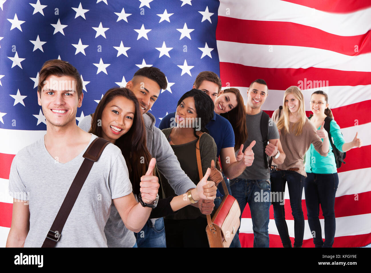 Gruppo di studenti diversi in piedi di fronte alla bandiera americana mostrando Thumb Up Foto Stock