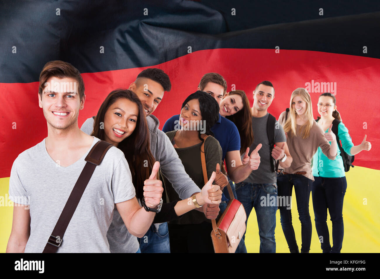 Gruppo di studenti multietnici in piedi di fronte alla bandiera tedesca mostrando Thumb Up Foto Stock