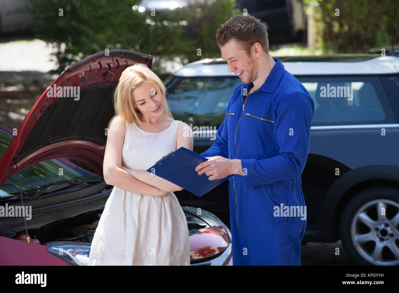 Giovanissimo meccanico che mostra appunti per clienti di sesso femminile da auto di rottura Foto Stock