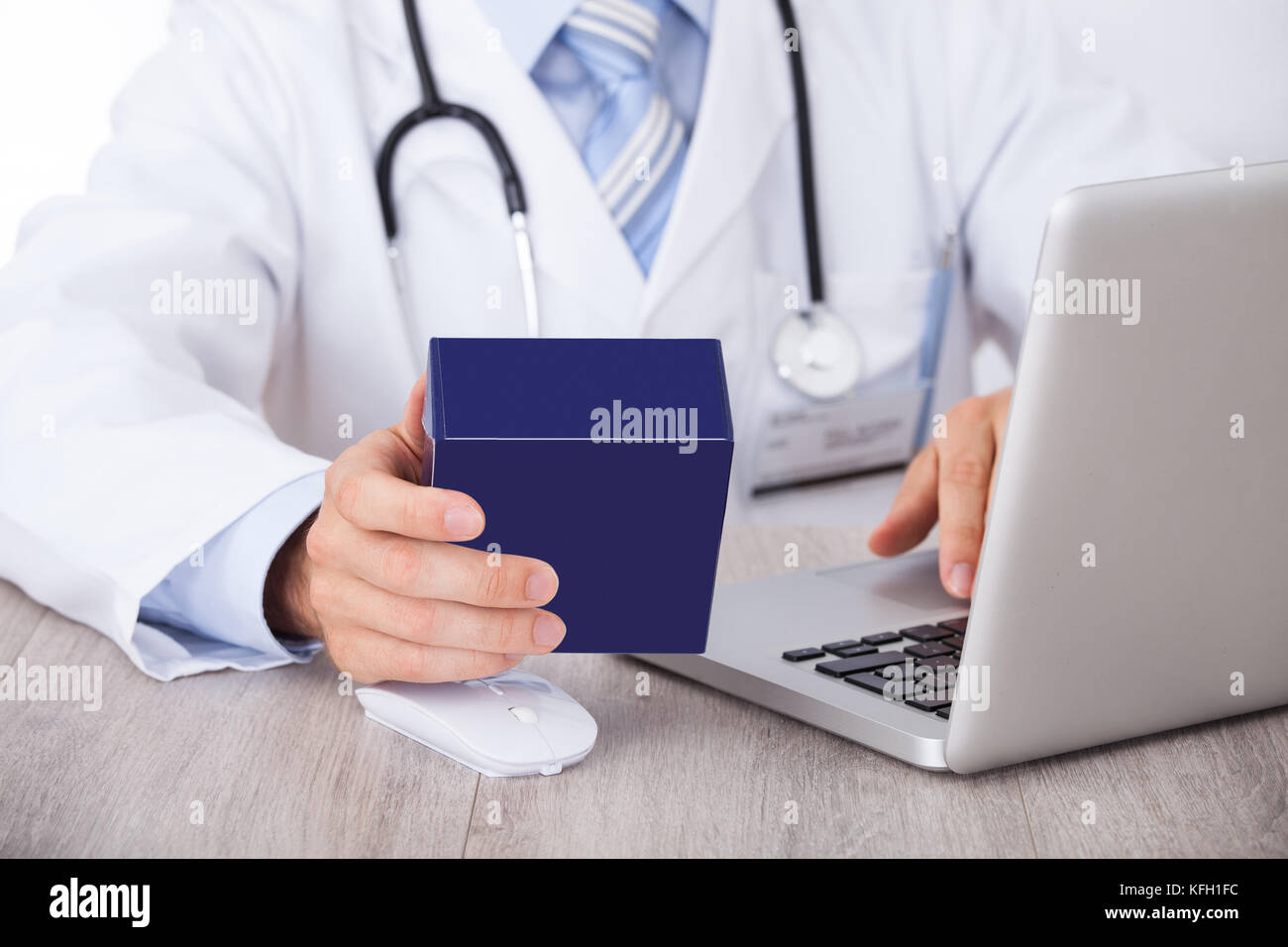 Sezione mediana del medico di medicina di contenimento box mentre utilizzando laptop in clinica Foto Stock