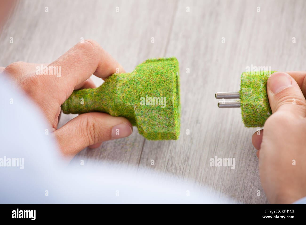 Immagine ritagliata di imprenditore tenendo coperto di erba spina elettrica e presa presso la scrivania in ufficio Foto Stock