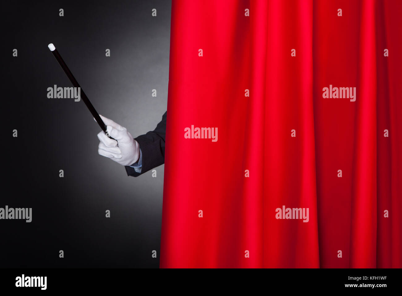 Immagine ritagliata di mago tenendo la bacchetta dietro il sipario di un palcoscenico Foto Stock