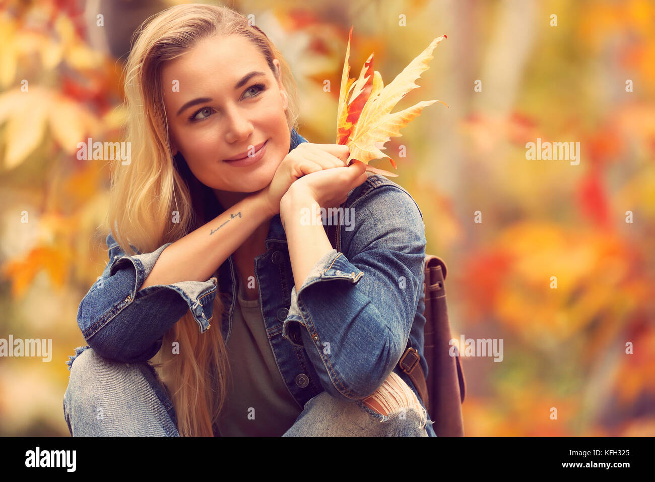 Ritratto di una bella donna seduta in autunno park a secco con foglie di acero in mano, godendo di un clima caldo e la bellezza della natura caduta Foto Stock