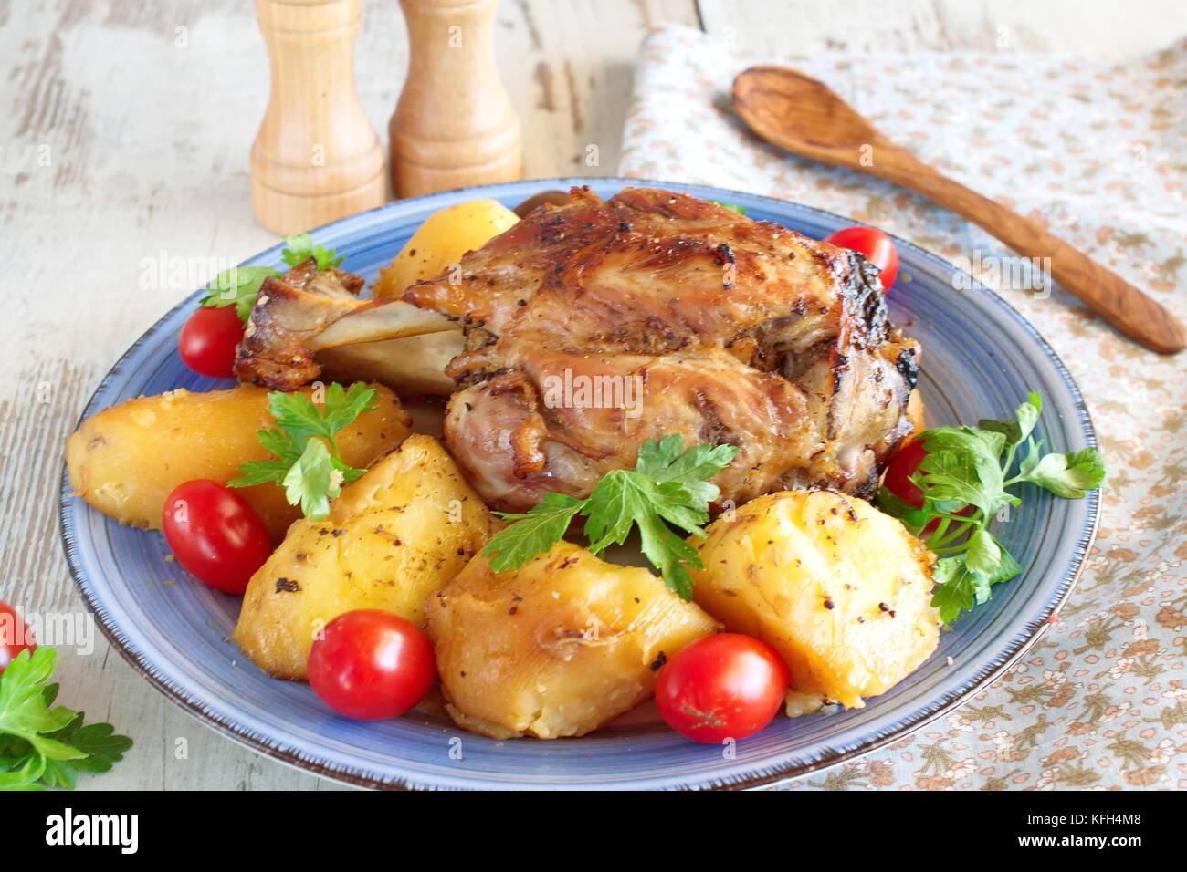 Cotto al forno lo stinco di maiale con patate, servita con prodotti freschi pomodori ciliegia e prezzemolo. Foto Stock