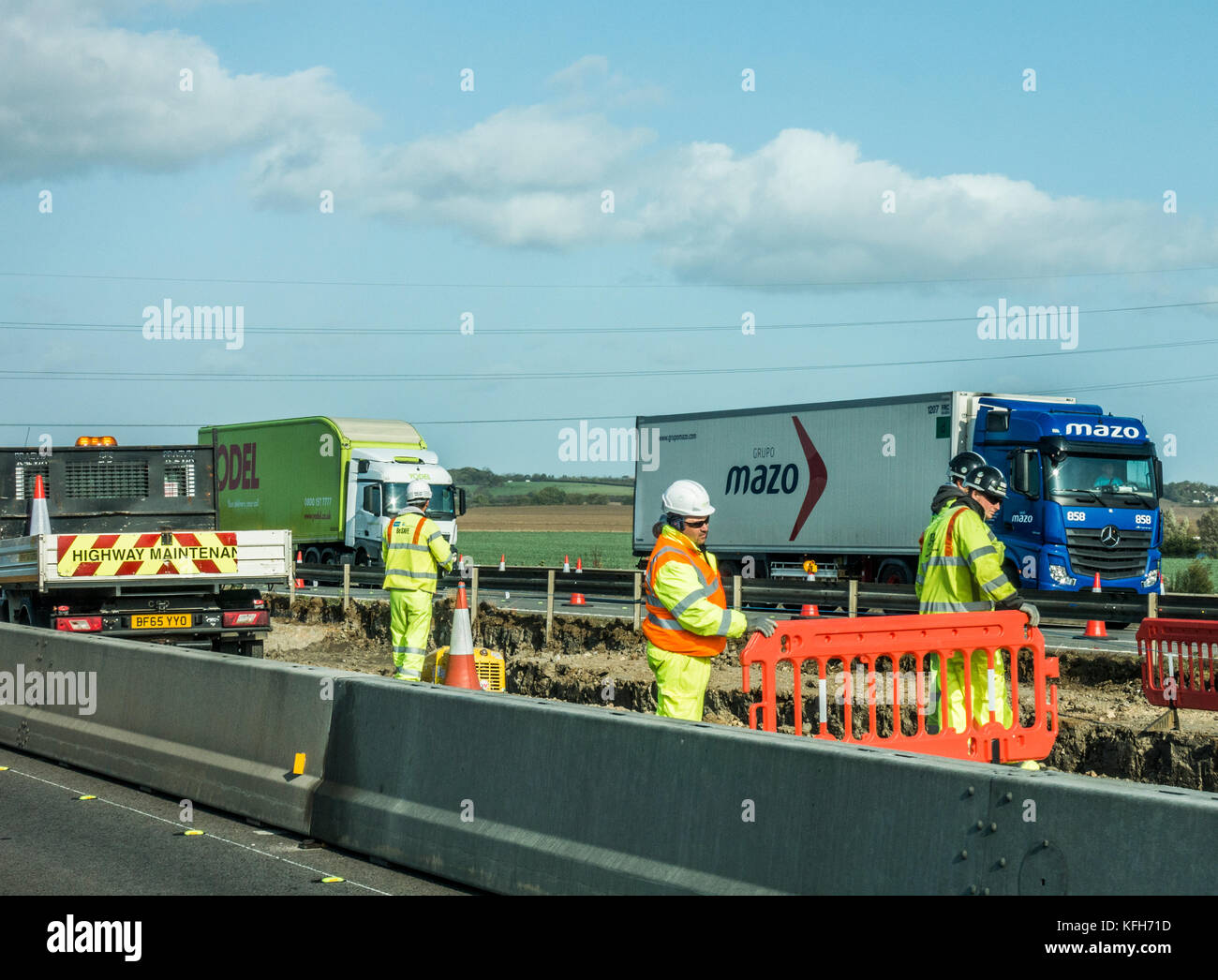 Equipaggio di manutenzione in giacche ad alta visibilità e duro cappelli, lavorando in prossimità di un foro nel centro di prenotazione della autostrada A1, a sud dell'Inghilterra, Regno Unito. Foto Stock