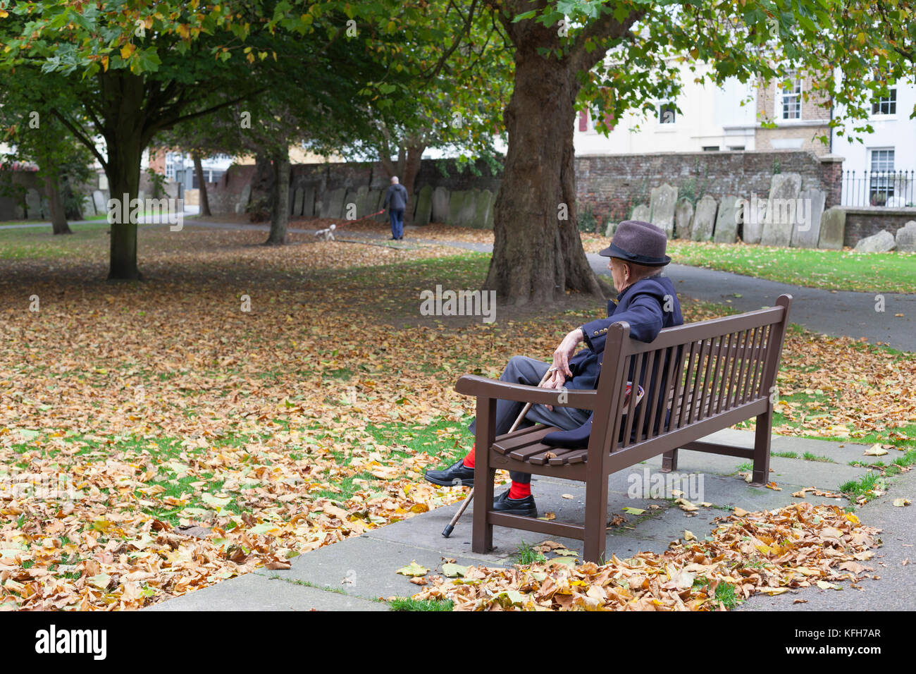 Il vecchio uomo seduto su un banco in un parco di San Giorgio chiesa trattativa con lapidi intorno al perimetro, trattare, Kent, England, Regno Unito, Europa Foto Stock