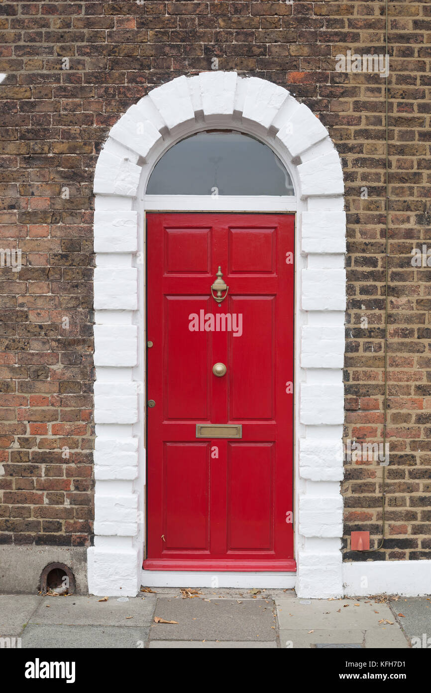Porta anteriore rossa con cartoniera e batticalcagno in oro e verniciata arco bianco e muro di mattoni Foto Stock Porta anteriore rossa con cartoniera e batticalcagno in oro e verniciata arco bianco e muro di mattoni Foto Stock