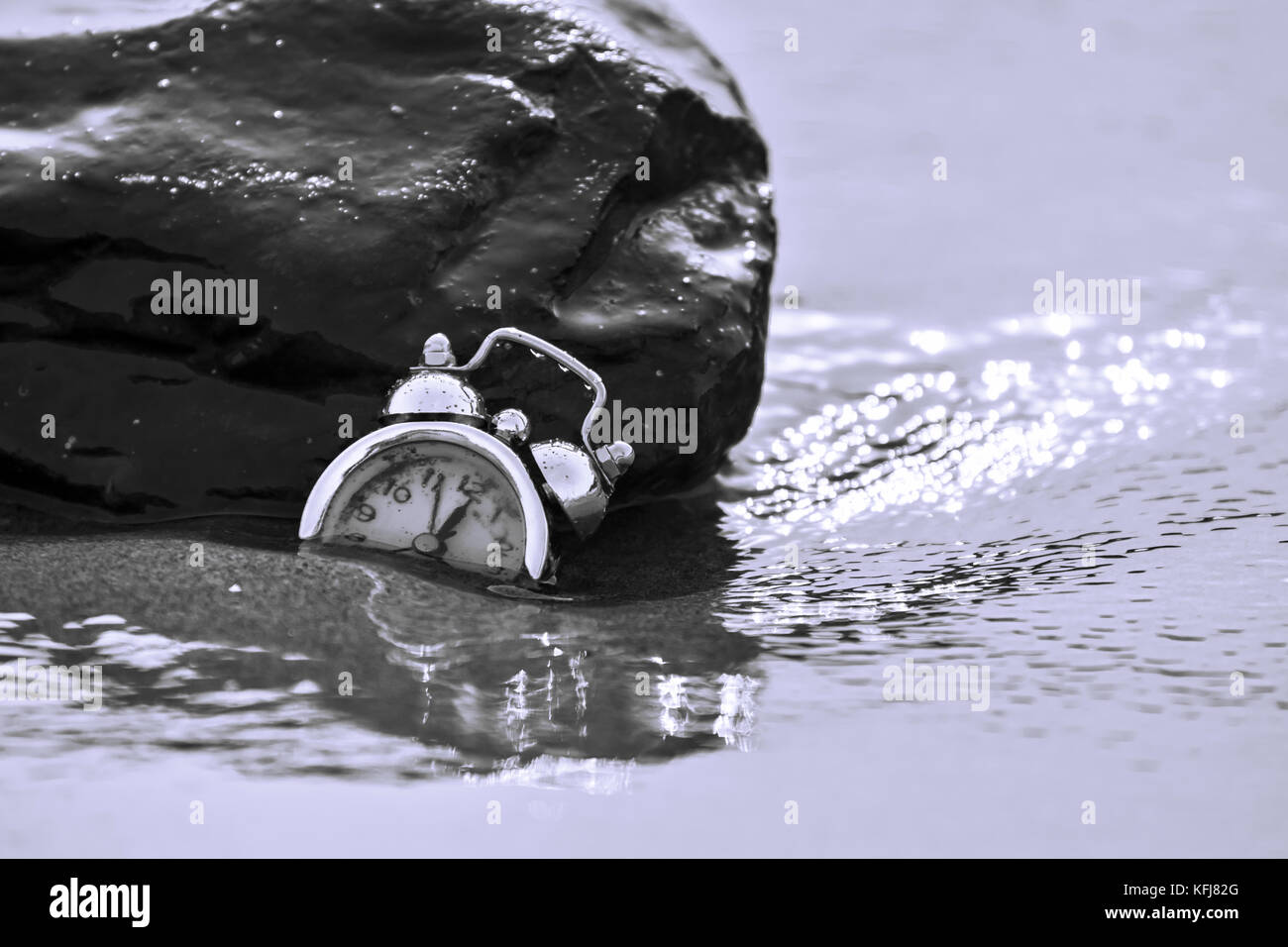 Un abstract consept colpo di un orologio che affonda nella sabbia circondata da acqua di mare correnti significato il passare del tempo Foto Stock