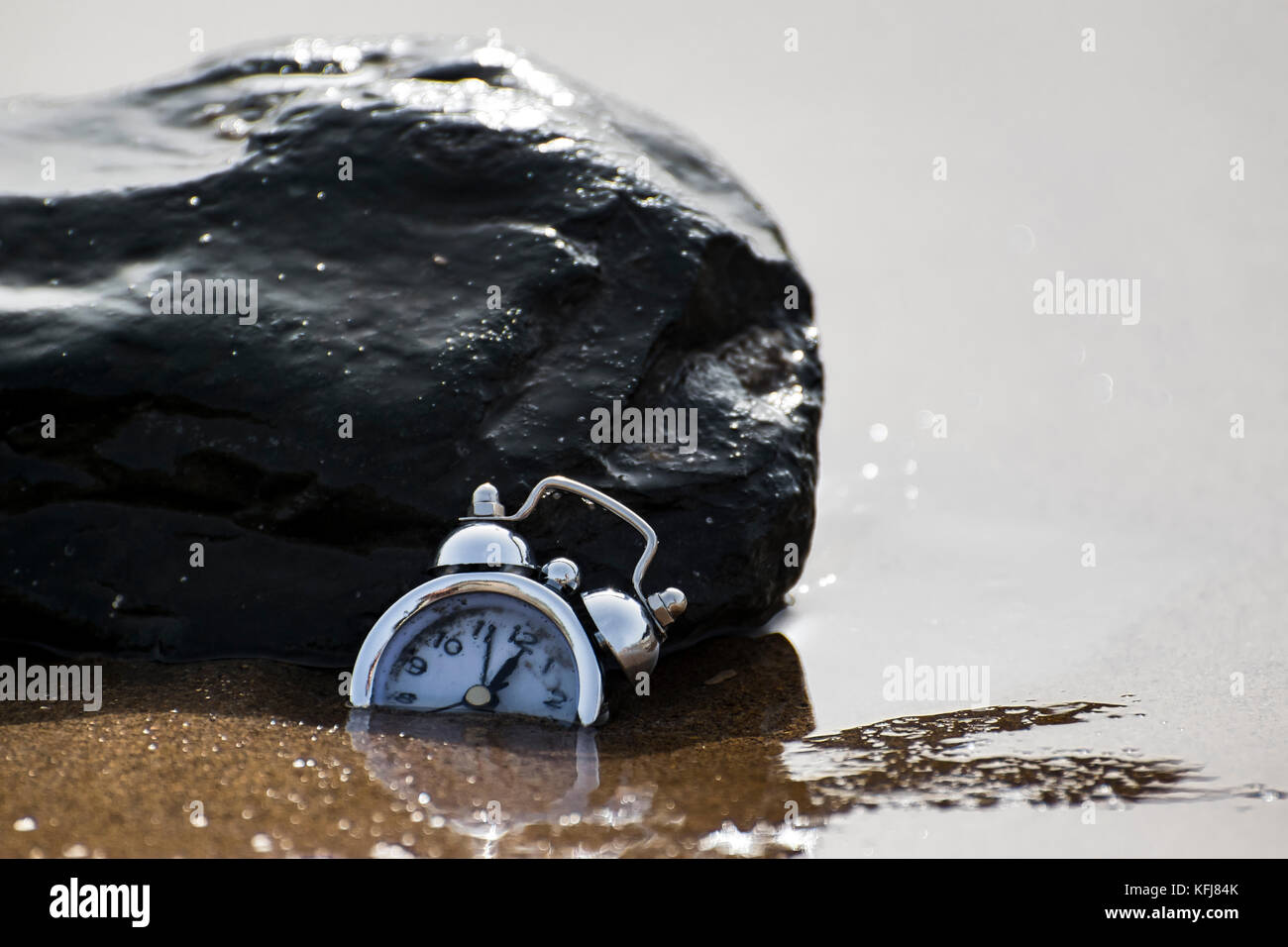 Un abstract consept colpo di un orologio che affonda nella sabbia circondata da acqua di mare correnti significato il passare del tempo Foto Stock
