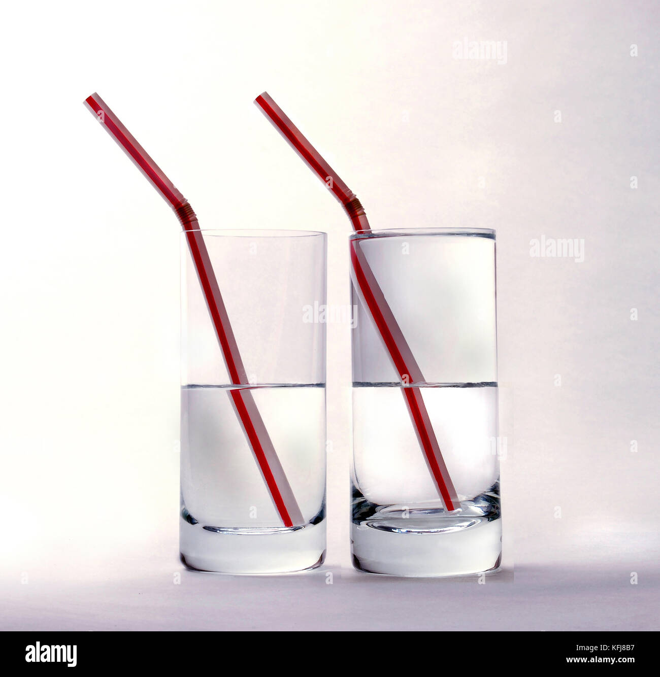 Due bicchieri mezzo pieno d'acqua, una metà inferiore, una metà superiore, con cannucce su sfondo bianco Foto Stock Due bicchieri mezzo pieno d'acqua, una metà inferiore, una metà superiore, con cannucce su sfondo bianco Foto Stock