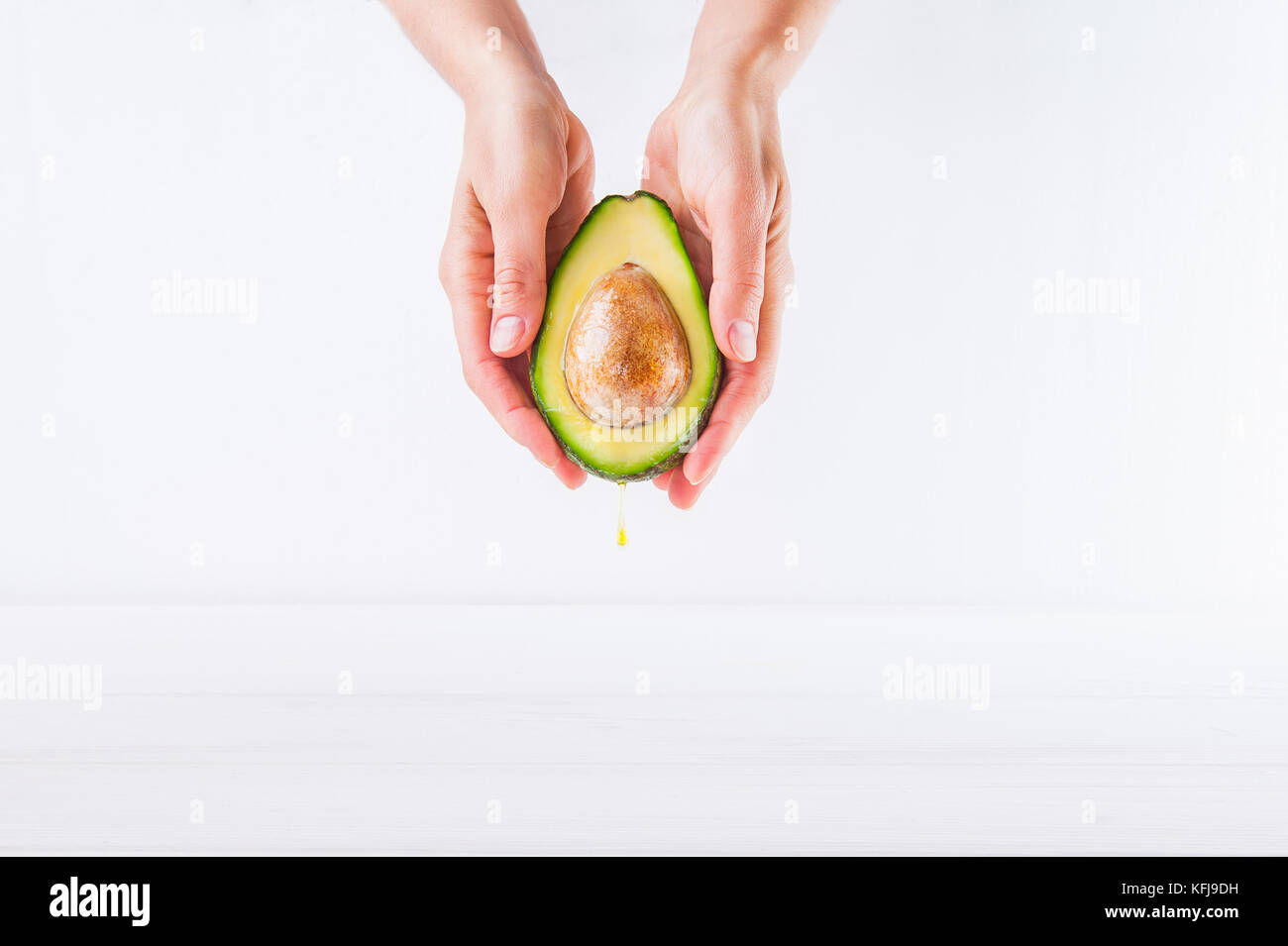 Fresh avocado con olio cadere in mani femminili sullo sfondo bianco isolato. sani e naturali di bellezza concetto. vista frontale. spazio per il testo Foto Stock