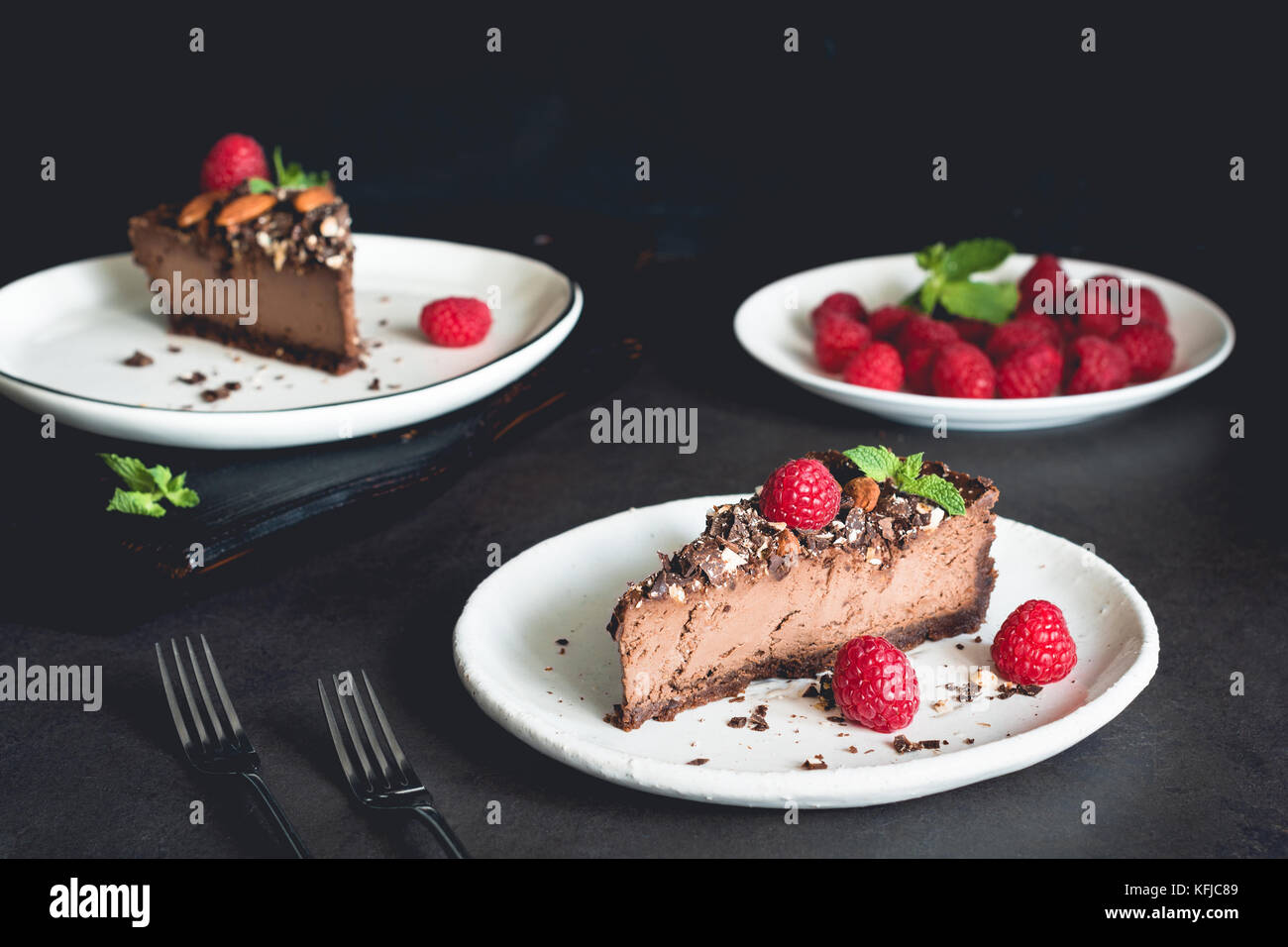 Due pezzi di cioccolato cheesecake decorate con lamponi e menta su piastra bianca su sfondo scuro. Foto Stock