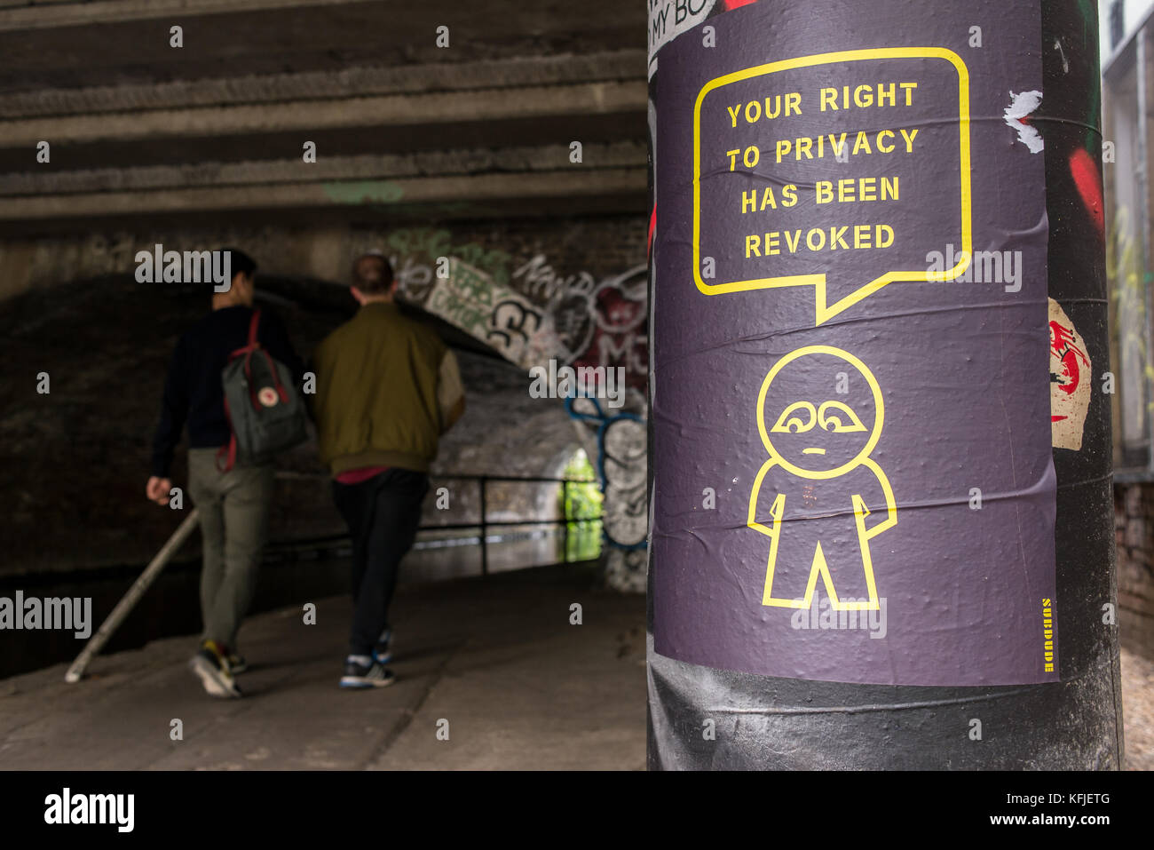 Street Art poster appeso su colonna nei pressi di un tunnel da artista subdude con uomo stilizzato e fumetti con slogan 'il tuo diritto alla privacy è stato revocato'. Foto Stock