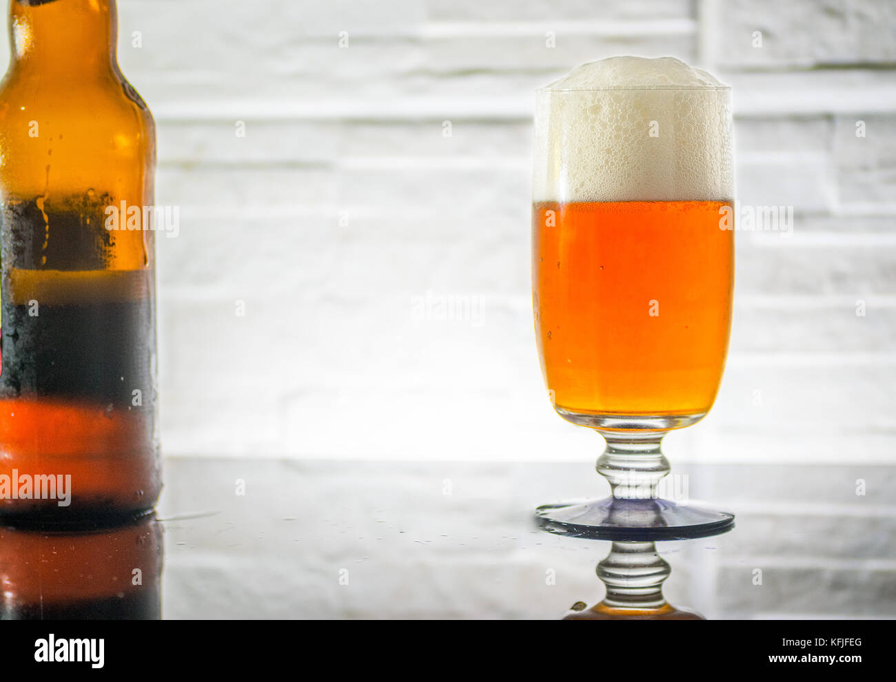 Bicchiere da birra, completa con la schiuma e la riflessione, robusto muro di pietra come sfondo e una bottiglia di barbabietola sul lato, retroilluminato Foto Stock