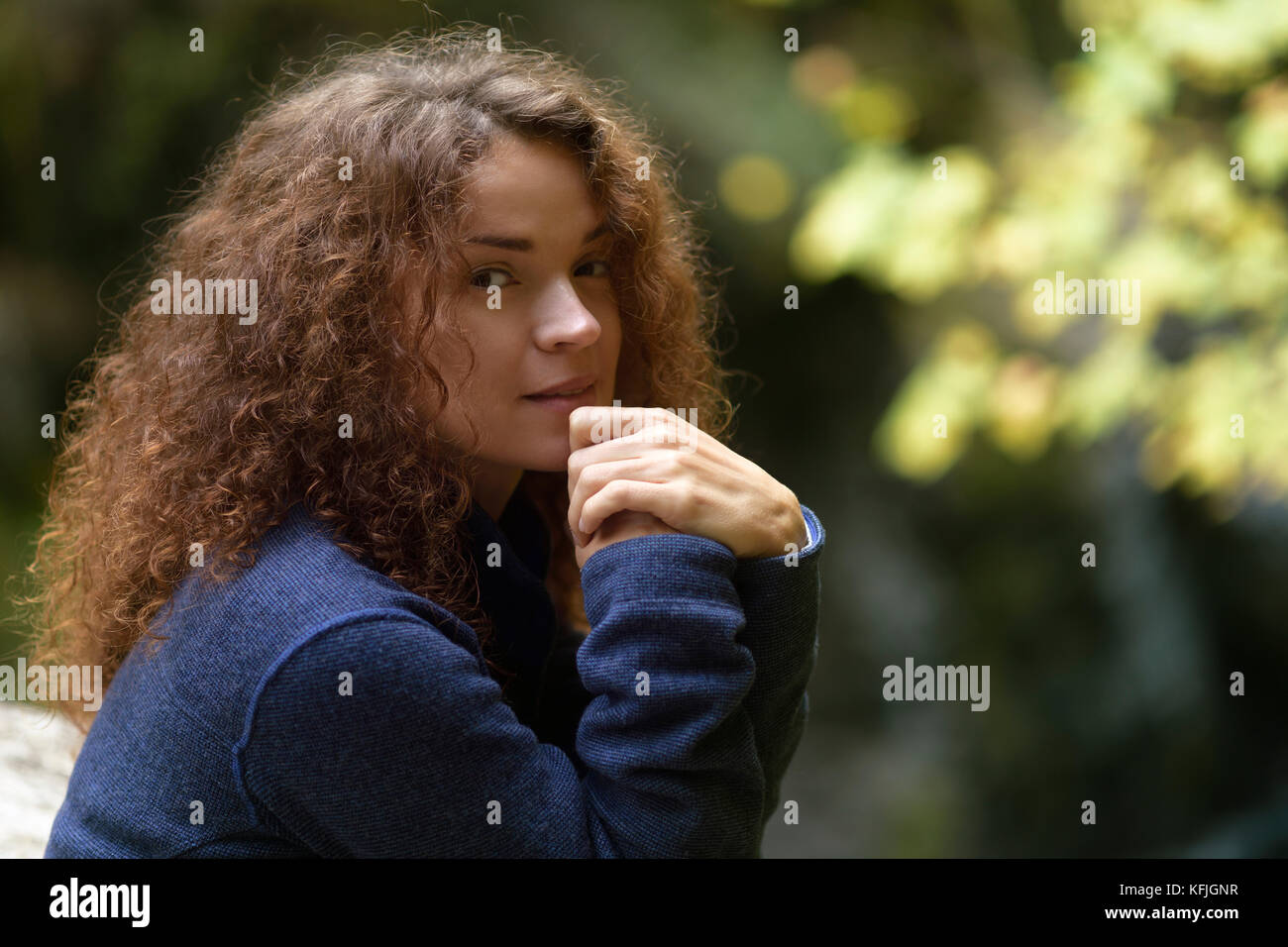 Candido ritratto naturale di una giovane donna con lunghi capelli castani ricci e tranquilla espressione di thoughtul sul suo volto in autunno scenario naturale Foto Stock