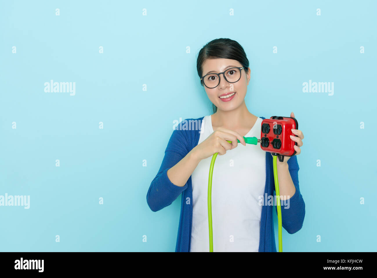 Sorridente donna felice con il tappo estrarre la presa che mostra il risparmio concetto elettrico isolato sulla parete blu sfondo con stile di vita di abbigliamento. Foto Stock